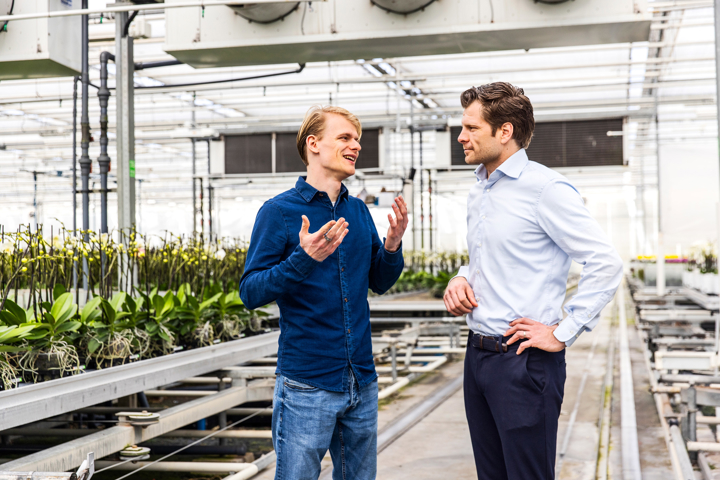 Twee mannen die met elkaar praten in een kas met orchideeën