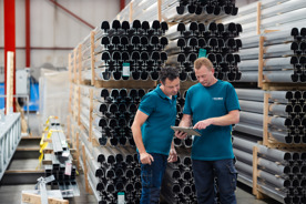 Two men look at a tablet with aluminum in the background