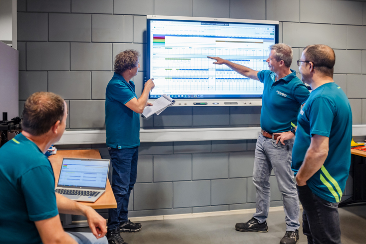 Group of men go over a schedule at a smart board and take notes